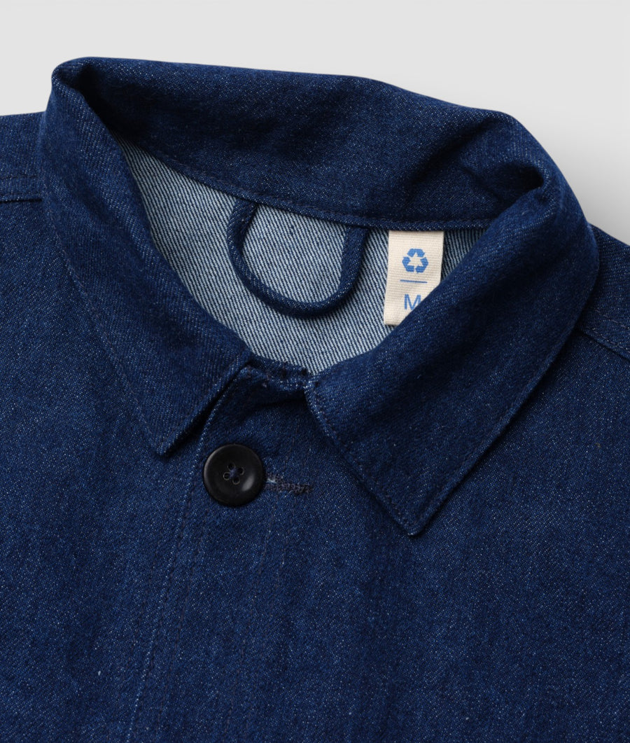 A close-up detail shot of a navy blue denim jacket with a recycling symbol on the tag - Industry of All Nations