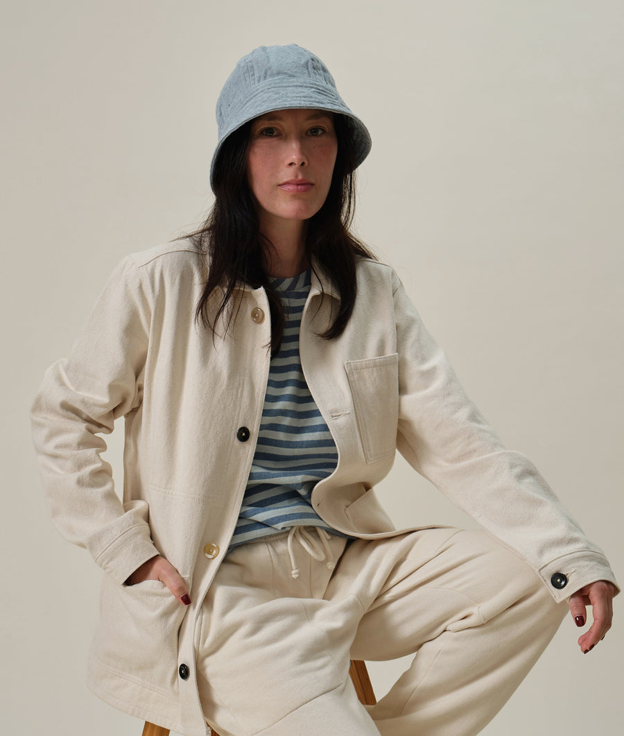 A woman wearing a cream-colored cotton jacket with buttons and pockets, paired with a striped shirt and gray bucket hat - Industry of All Nations