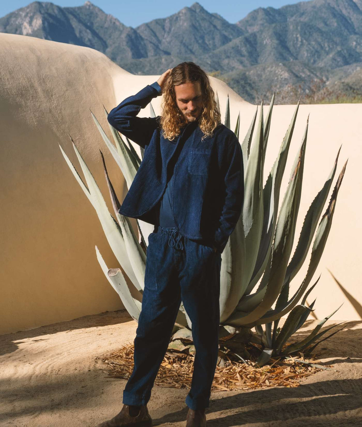 Blue denim jumpsuit worn by model in desert landscape with mountains in background - Industry of All Nations