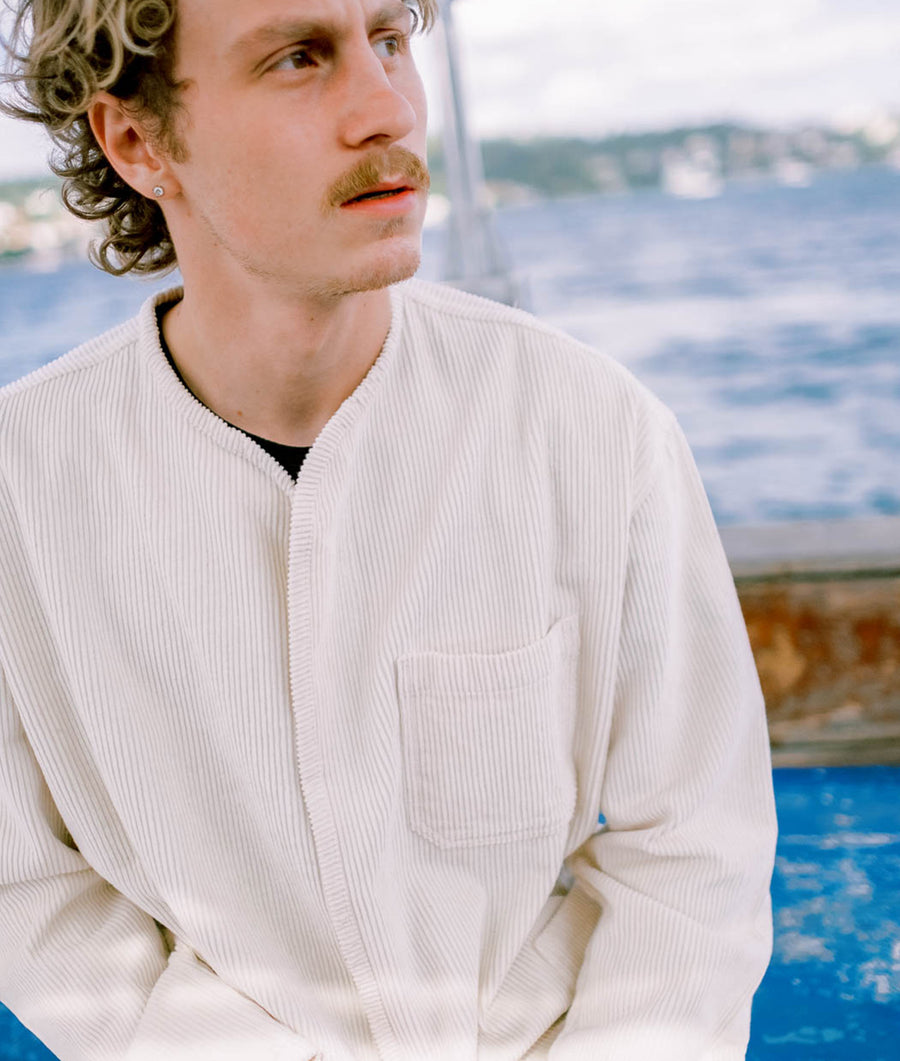 White ribbed cotton jacket worn by model against a backdrop of a scenic body of water - Industry of All Nations