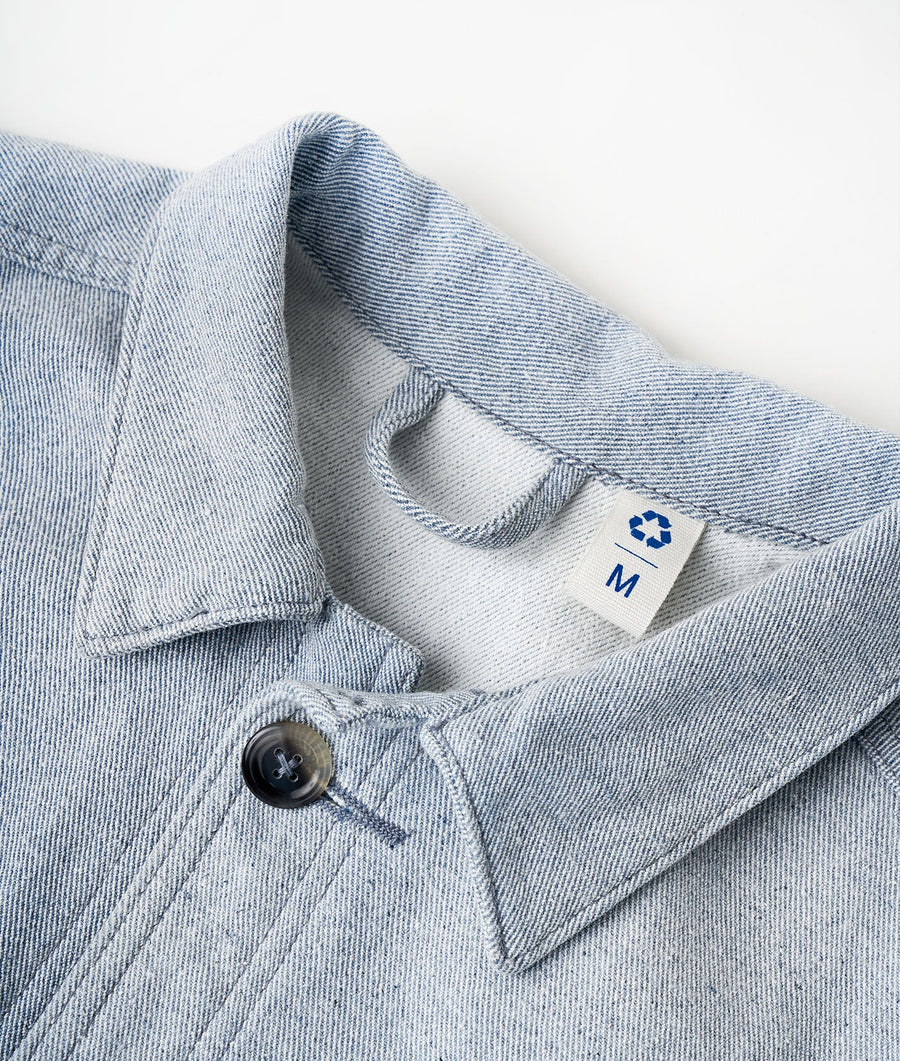 Folded denim blue chambray button-up shirt with recycling symbol patch on sleeve - Industry of All Nations