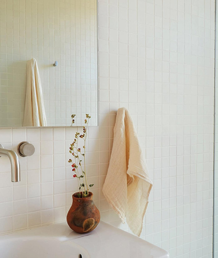 Beige towel folded neatly on a white tiled bathroom counter, with a small potted plant beside it - Industry of All Nations