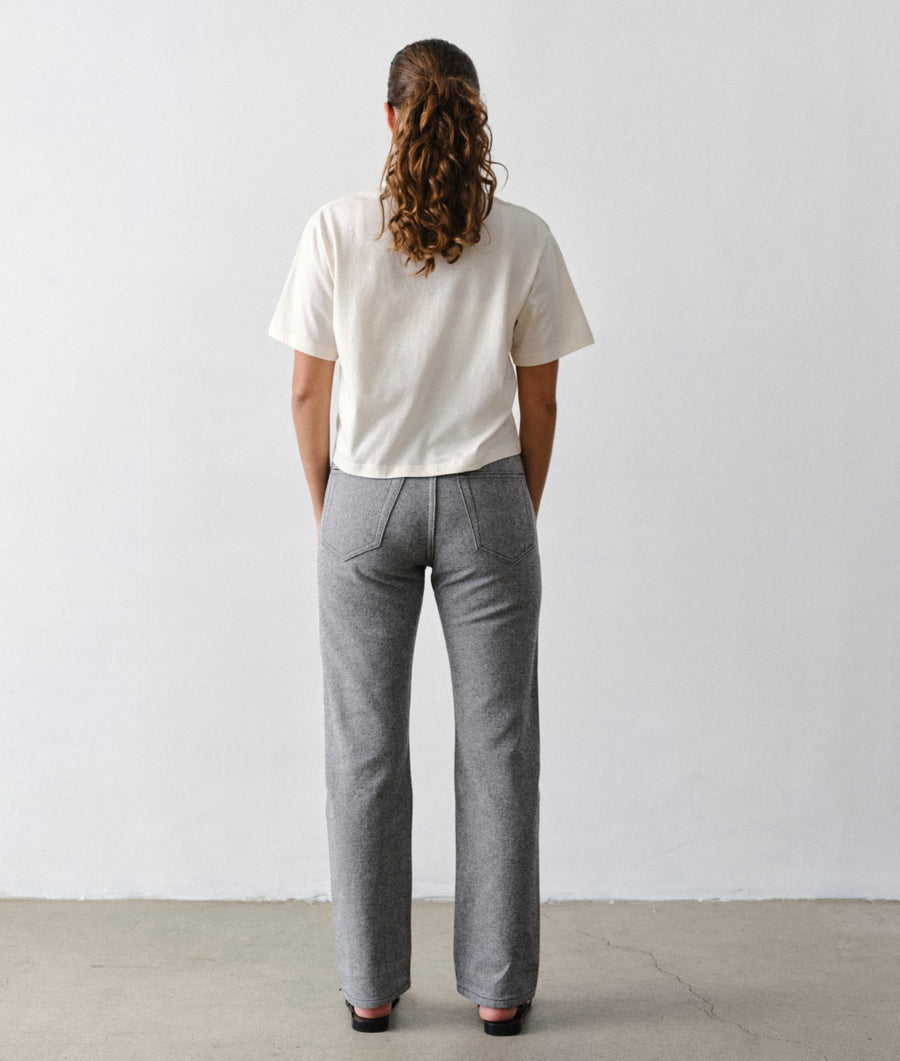Back view of a woman wearing the IOAN New Jeans in Charcoal with an Undyed Cropped T-Shirt against a light gray studio background.