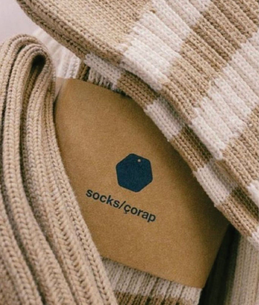 Close-up of IOAN undyed organic cotton and off-white striped knit socks with a brown paper tag featuring the IOAN logo and “socks/čorap” text.