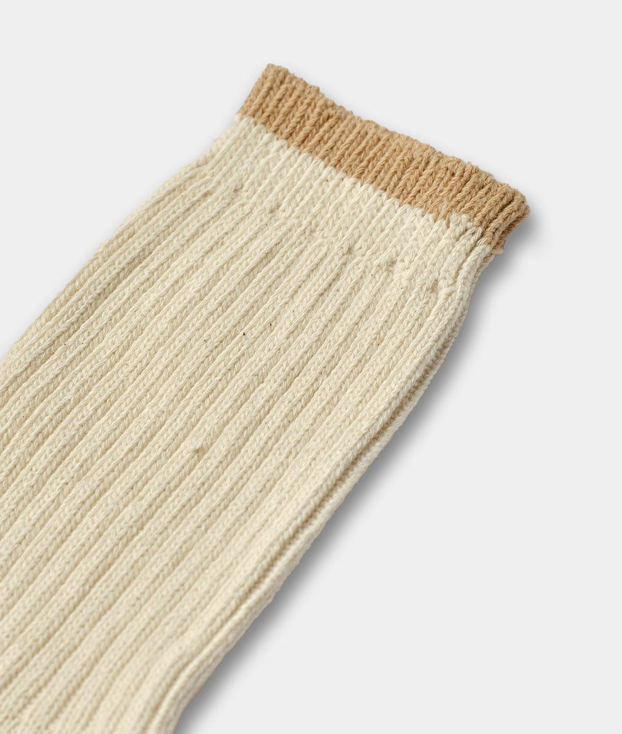 A close-up of a ribbed knit sock in cream with a contrasting tan cuff, shown against a light gray background.
