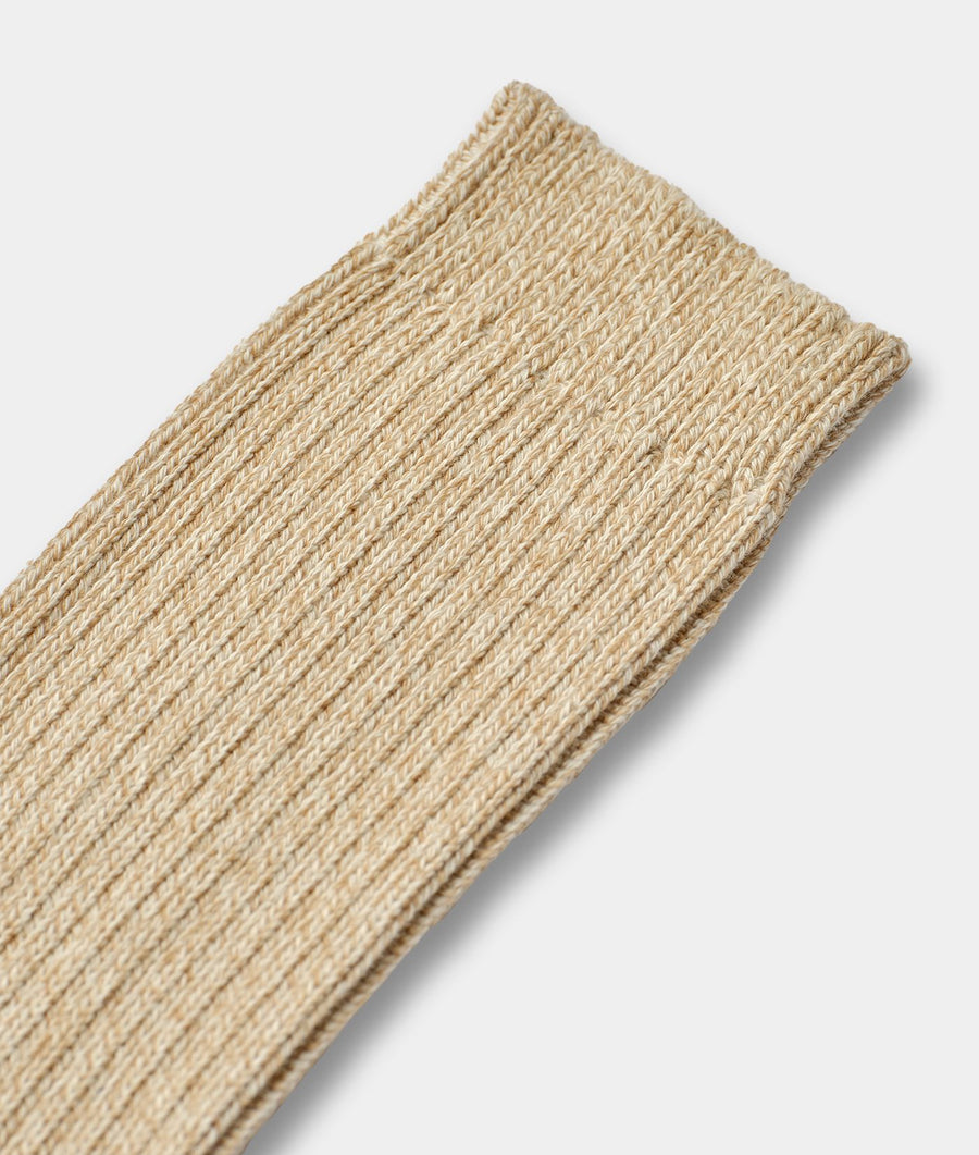 Close-up of an IOAN Organic Cotton Sock in a natural beige color, showing the detailed ribbed knit texture of the yarn and cuff against a light gray background.