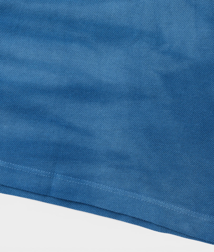 Blue cotton shirt made by Industry of All Nations, shown in a close-up flat lay detail shot - Industry of All Nations