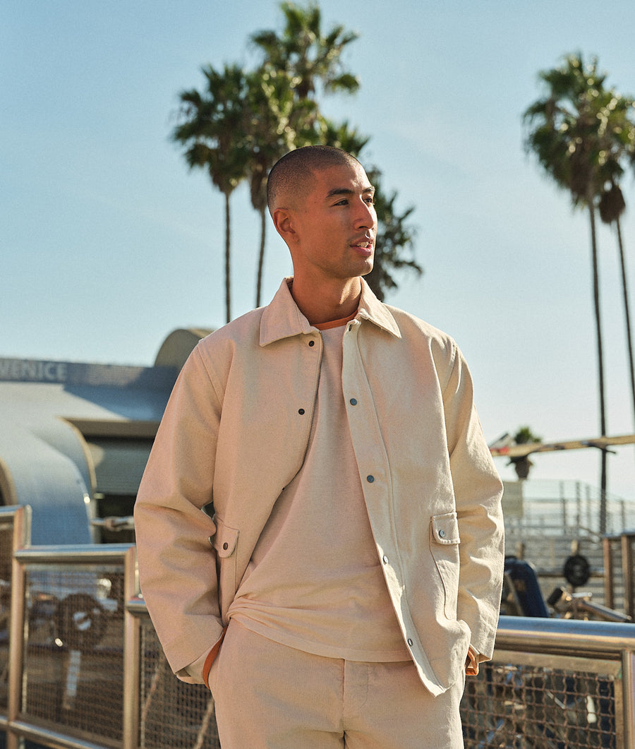 A person wearing a beige jacket and matching pants, standing in front of palm trees - Industry of All Nations