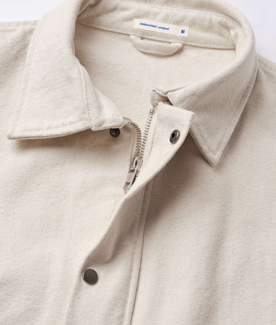 A close-up detail shot of a cream-colored, unbleached, undyed organic cotton sweatshirt with a zipper closure - Industry of All Nations