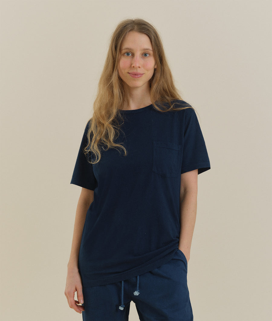 Woman wearing a navy blue t-shirt with a chest pocket, standing against a light colored background - Industry of All Nations