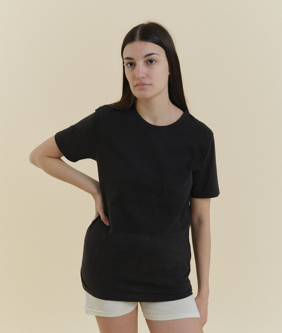 A young woman wearing a black crew neck t-shirt, standing against a cream-colored backdrop - Industry of All Nations