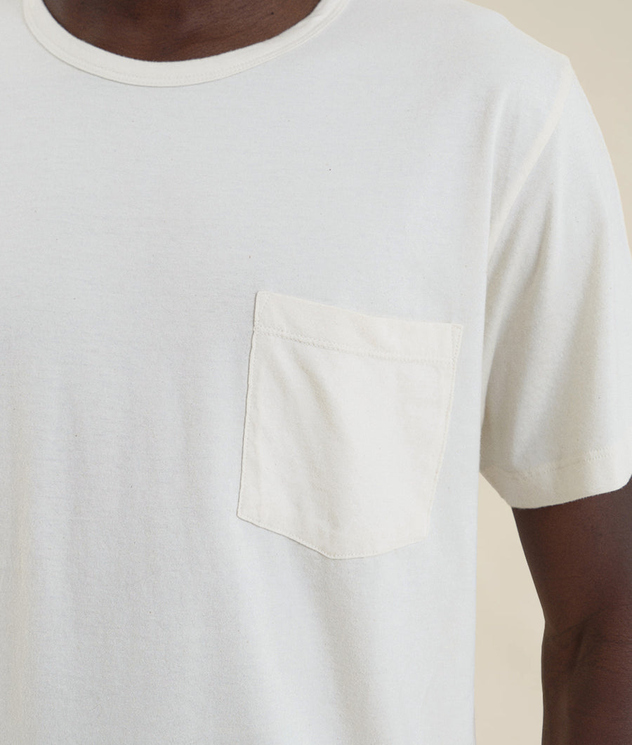 A close-up view of a white, organic cotton t-shirt with a small pocket on the front, worn by a model - Industry of All Nations