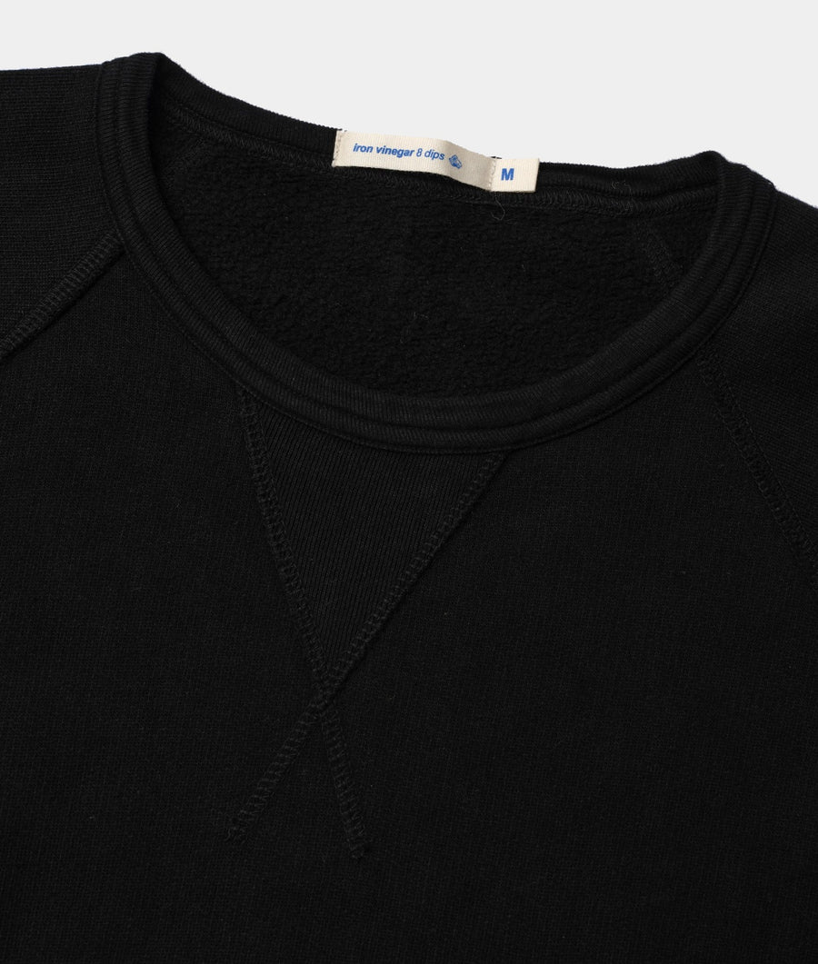 Close-up shot of a black short-sleeved t-shirt with a fabric care tag attached - Industry of All Nations