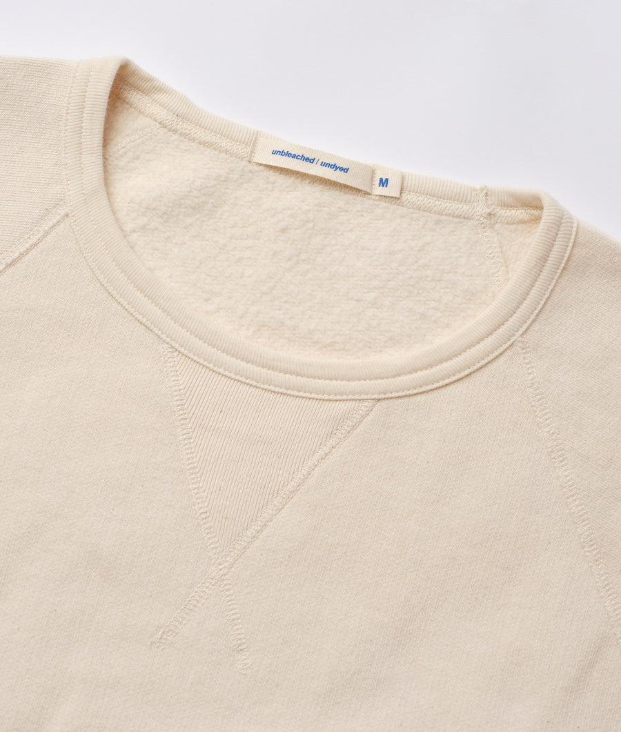 Close-up detail shot of a cream-colored, unbleached and undyed cotton crewneck sweater with a size M label - Industry of All Nations