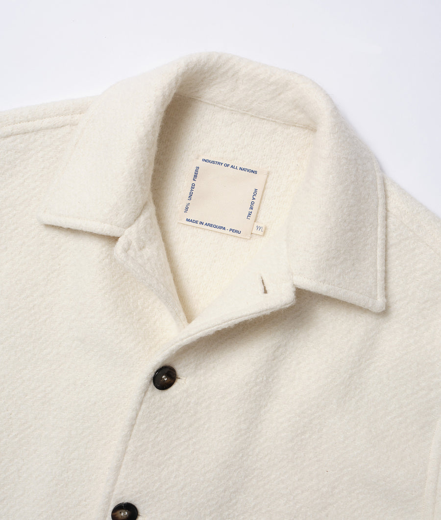 Flat lay image of a cream-colored alpaca wool sweater with the "Industry of All Nations" brand label - Industry of All Nations