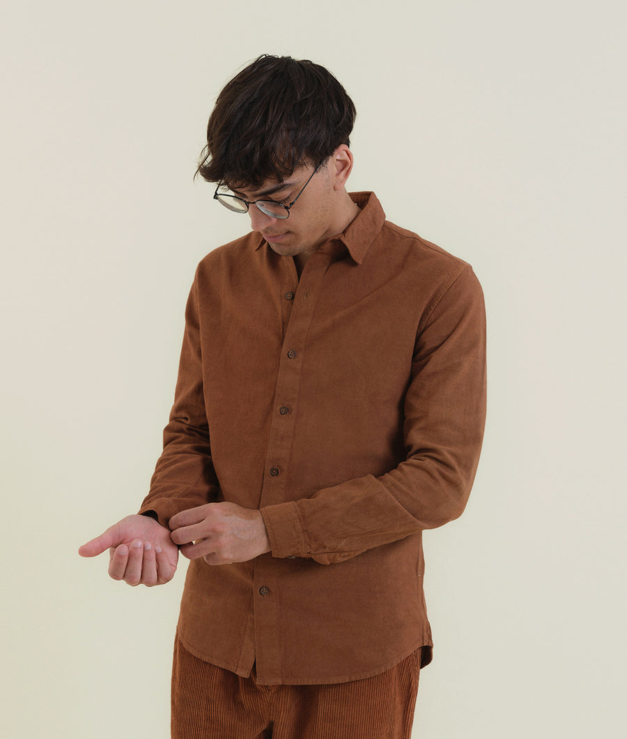 A man wearing a brown corduroy shirt with a button-down collar and long sleeves, standing against a white background - Industry of All Nations