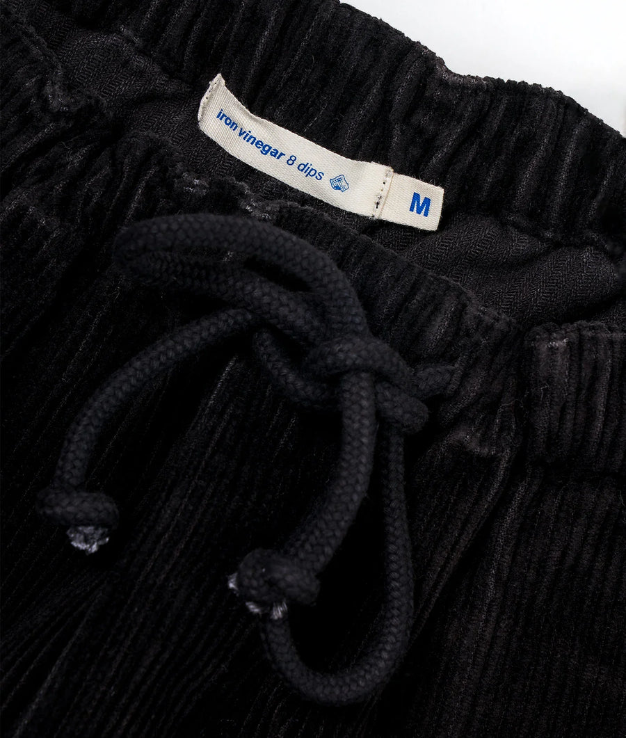 A close-up detail shot of a black, pleated garment with a size tag that reads 'M' - Industry of All Nations