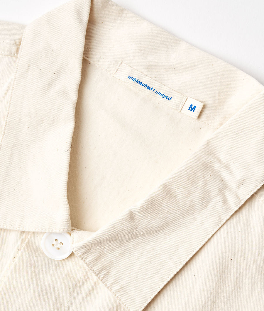 Flat lay image of a white, unbleached, uncleyed cotton shirt with an 'M' size tag - Industry of All Nations