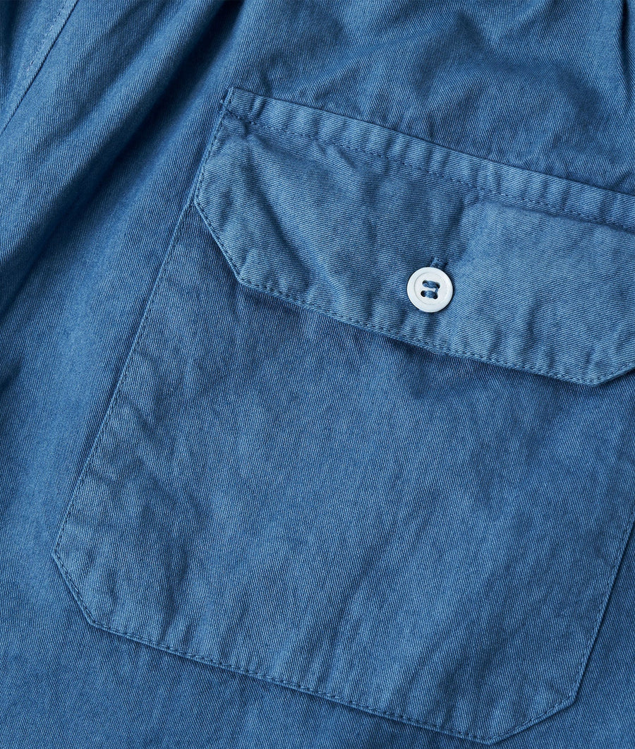 A close-up detail shot of a navy blue denim jacket with a white button on the chest pocket. - Industry of All Nations