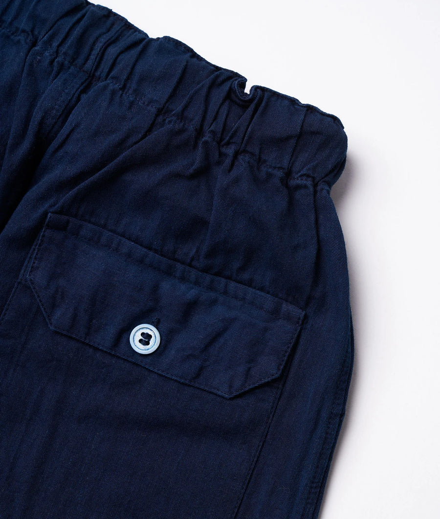 A close-up detail shot of a navy blue pair of pants with a button pocket and elastic waistband from Industry of All Nations.