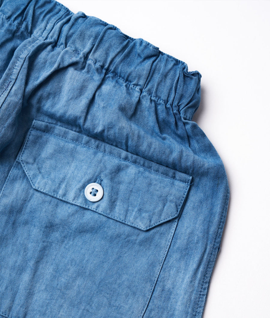 Close-up shot of a blue cotton denim pant with a single chest pocket and button closure - Industry of All Nations