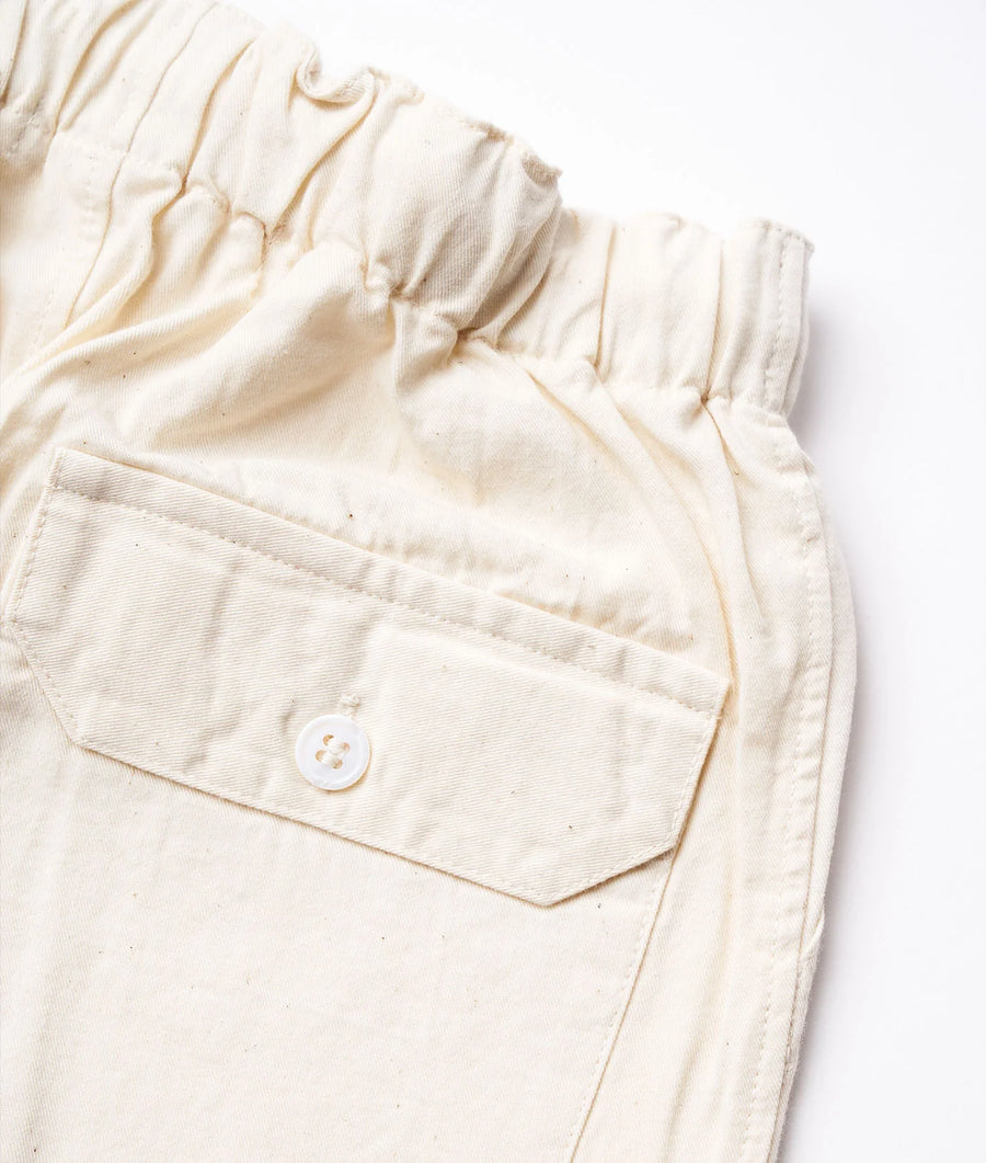 Flat lay detail shot of a cream-colored organic cotton worker jacket with a front pocket - Industry of All Nations