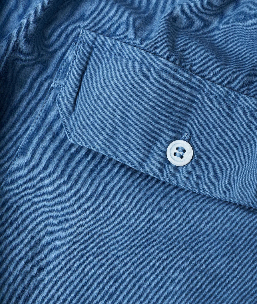 A close-up detail shot of a deep blue denim shirt pocket with a white button - Industry of All Nations
