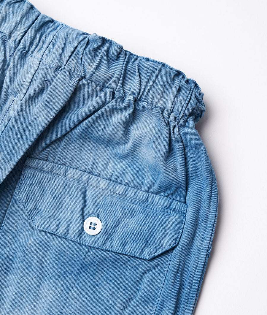 A close-up of the front pocket and waistband of a pair of blue cotton cargo pants laid flat - Industry of All Nations