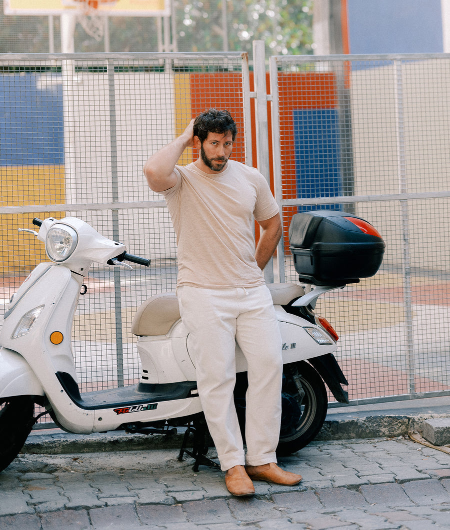 Beige t-shirt and pants worn by a man sitting on a white scooter in front of a colorful background - Industry of All Nations