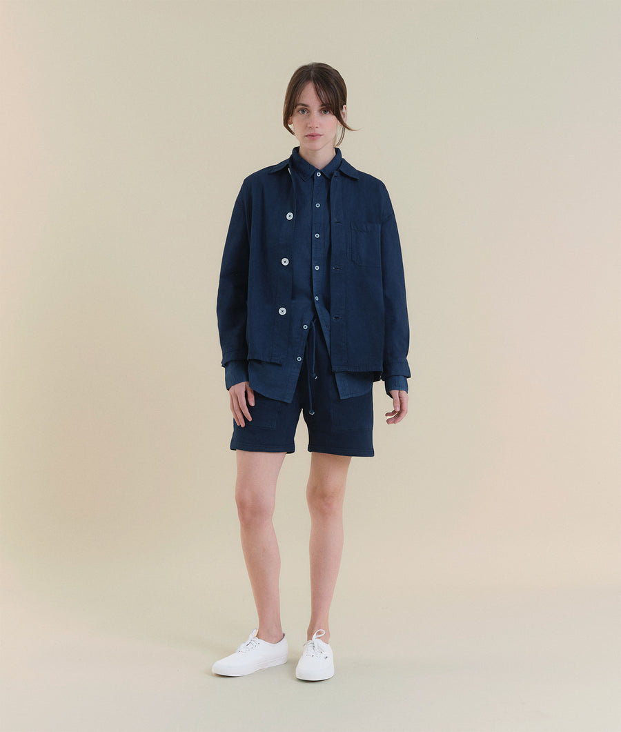A woman wearing a navy blue utility jacket and shorts, standing against a beige background - Industry of All Nations