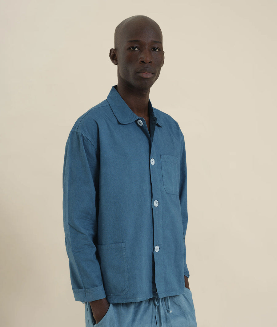 A man wearing a blue button-up shirt from the Industry of All Nations sustainable apparel brand.