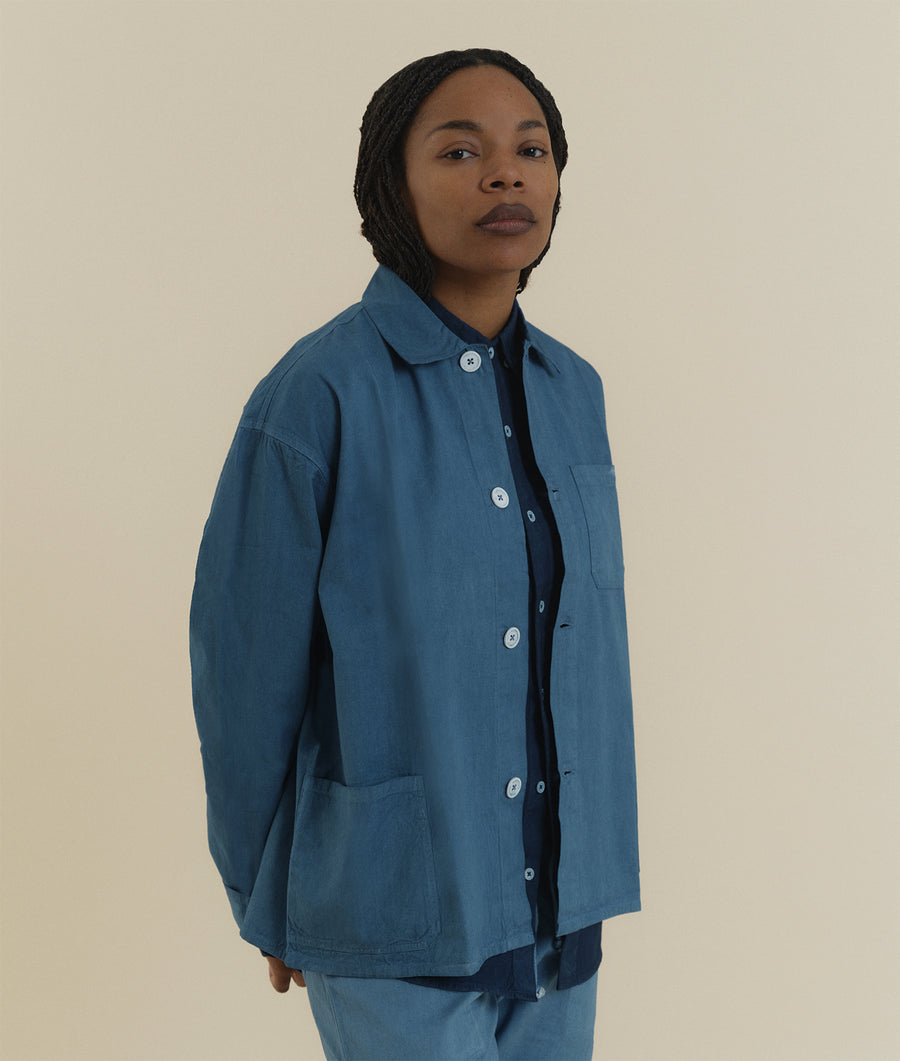 A woman wearing a blue denim jacket with buttons, standing against a cream background - Industry of All Nations