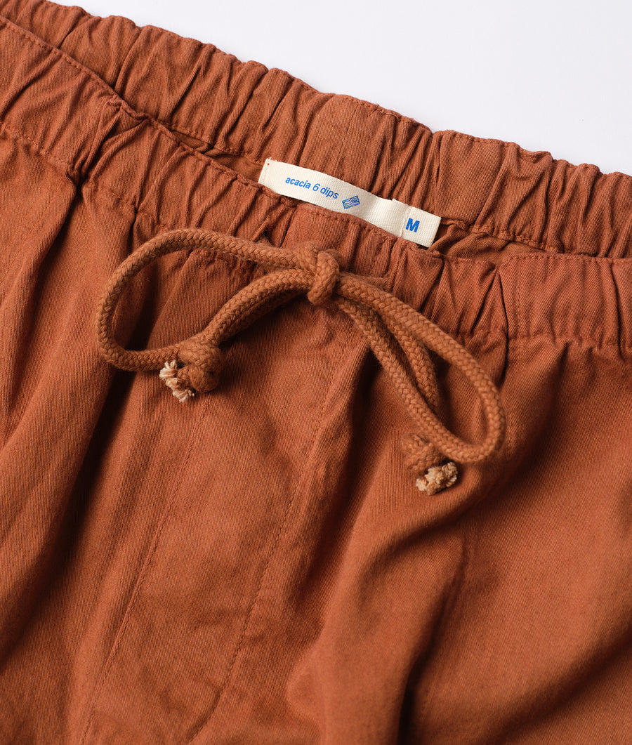Detail shot of a rust-colored, drawstring waist shorts made of organic cotton by Industry of All Nations.