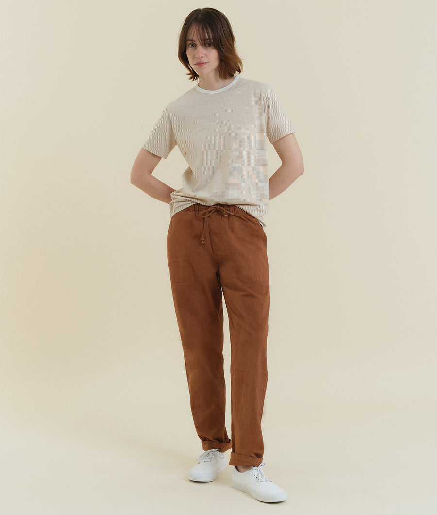A person wearing a beige striped crewneck t-shirt and brown drawstring pants, standing in white sneakers - Industry of All Nations