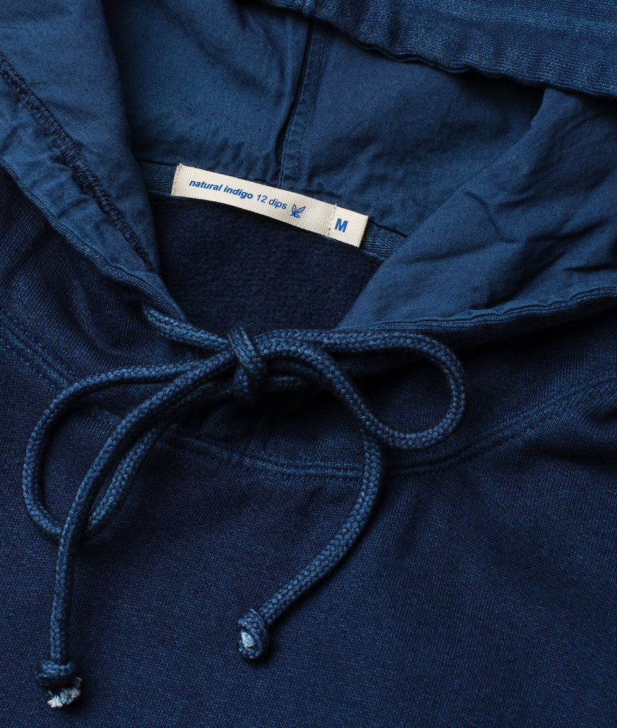 A close-up detail shot of a navy blue indigo-dyed cotton drawstring pullover hoodie from Industry of All Nations.