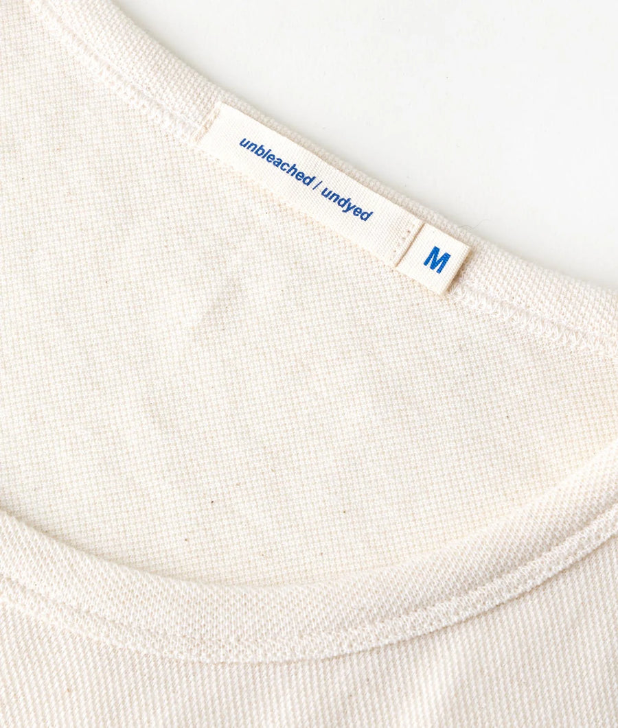 Close-up detail shot of a beige, unbleached and undyed cotton t-shirt from Industry of All Nations.