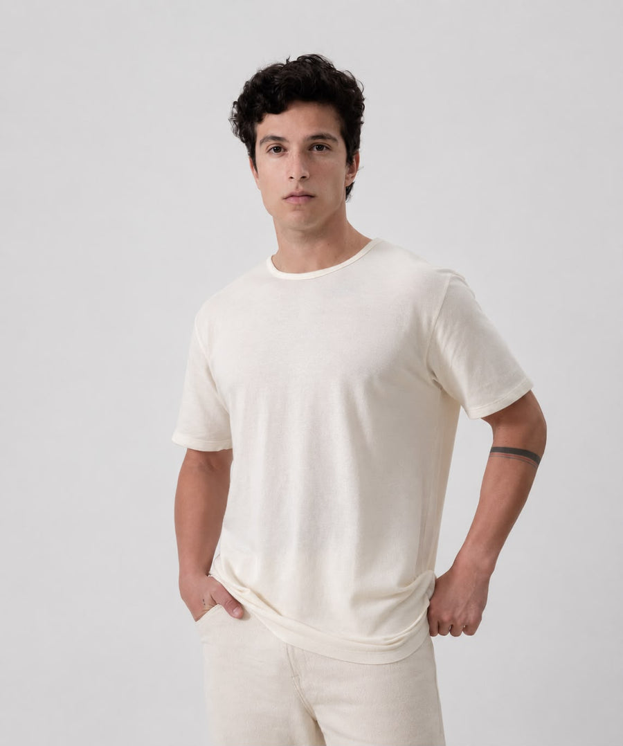 A man wearing  IOAN Pique Crewneck T-shirt and matching undyed pants, standing against a light gray studio background.