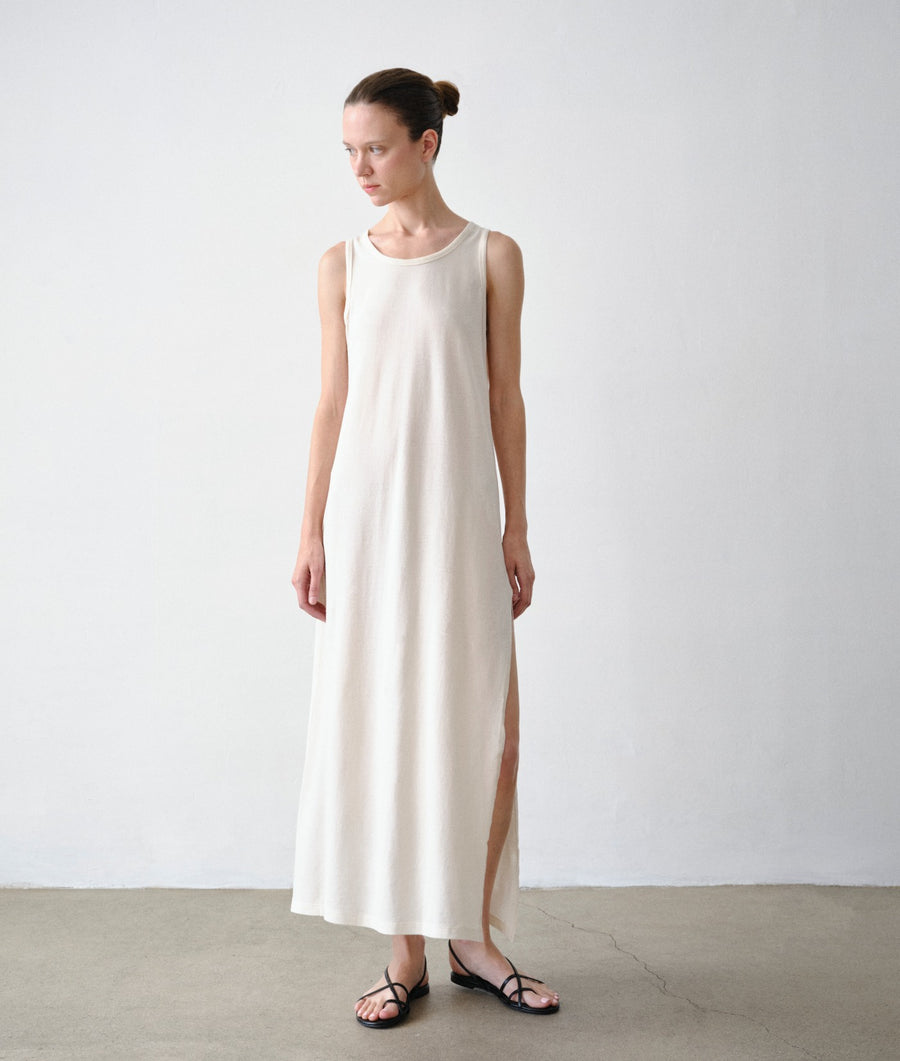 A woman modeling IOAN Pique Tank dress with a side slit, standing against a plain light gray wall and concrete floor.