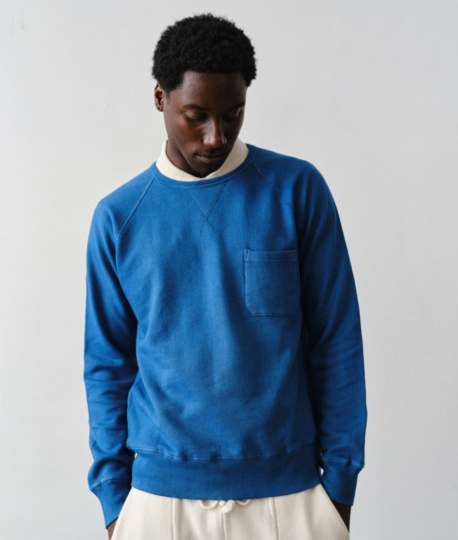 Man wearing the IOAN Pocket Sweatshirt in Indigo 6 layered over a white t-shirt and paired with IOAN Super Sweatpants in cream against a neutral light gray background.