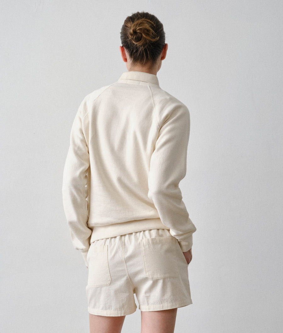 Back view of a model wearing an IOAN undyed long-sleeve crewneck sweatshirt and matching drawstring shorts against a plain light gray studio background.