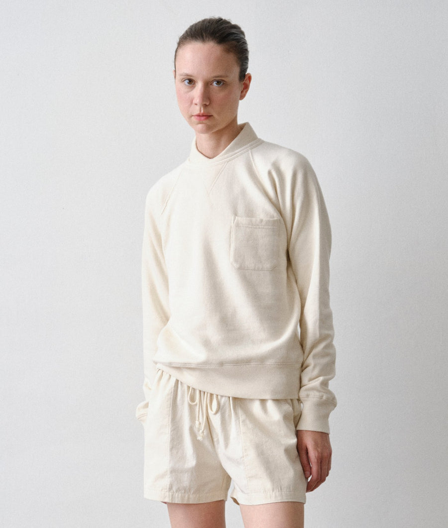 Model wearing an IOAN undyed long-sleeve crewneck sweatshirt and matching drawstring shorts against a plain light gray studio background.