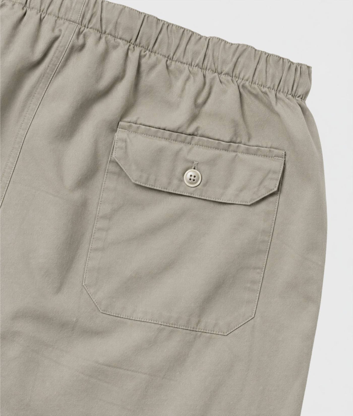 Close-up of a pair of light khaki trousers showing the elastic waistband and a buttoned flap pocket.