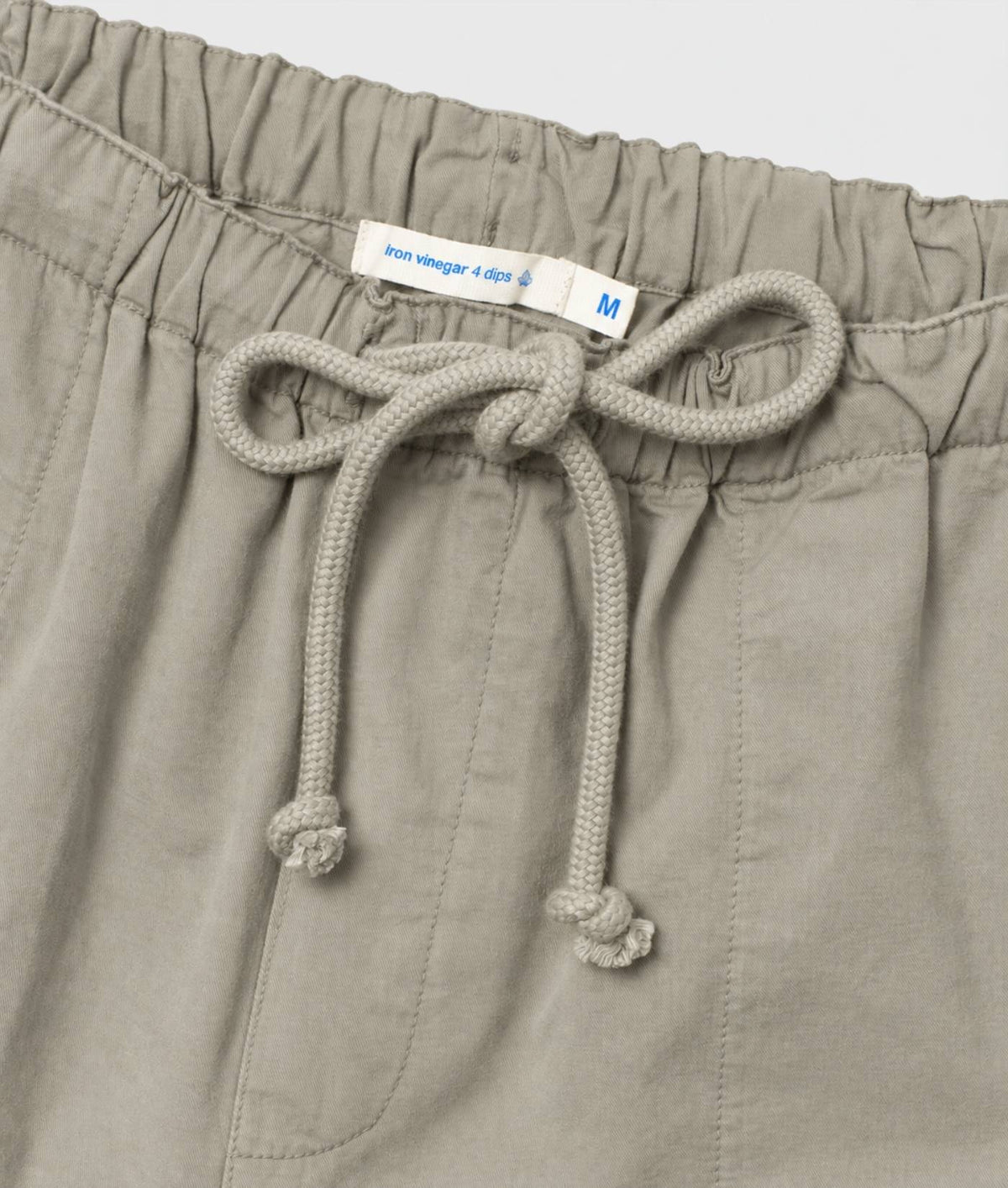 Close-up of a pair of light gray drawstring pants showing the elastic waistband, textured drawstring, and a white size tag.