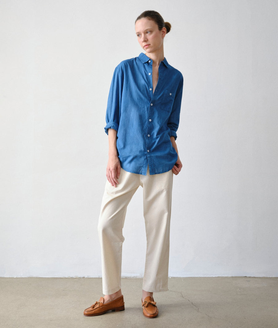 Model standing in a minimalist studio wearing the IOAN Madras Shirt in Indigo 6, IOAN Ponya Drawstring Pants, and brown leather loafers.