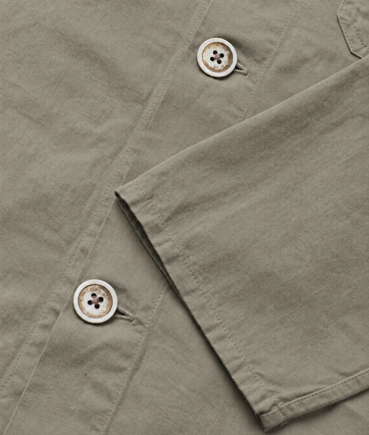 Close-up of a light olive green shirt fabric showing the texture, a buttoned collar, and a buttoned cuff.