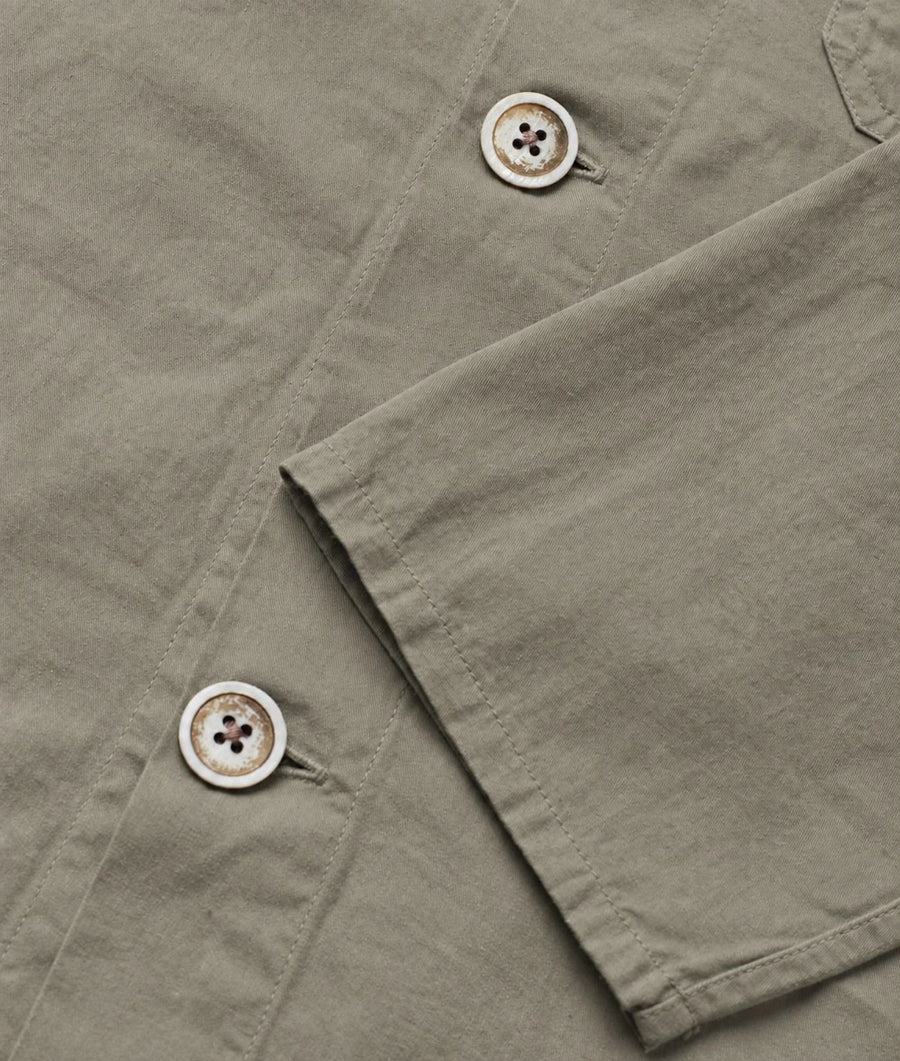 Close-up of a light olive green shirt fabric showing the texture, a buttoned collar, and a buttoned cuff.