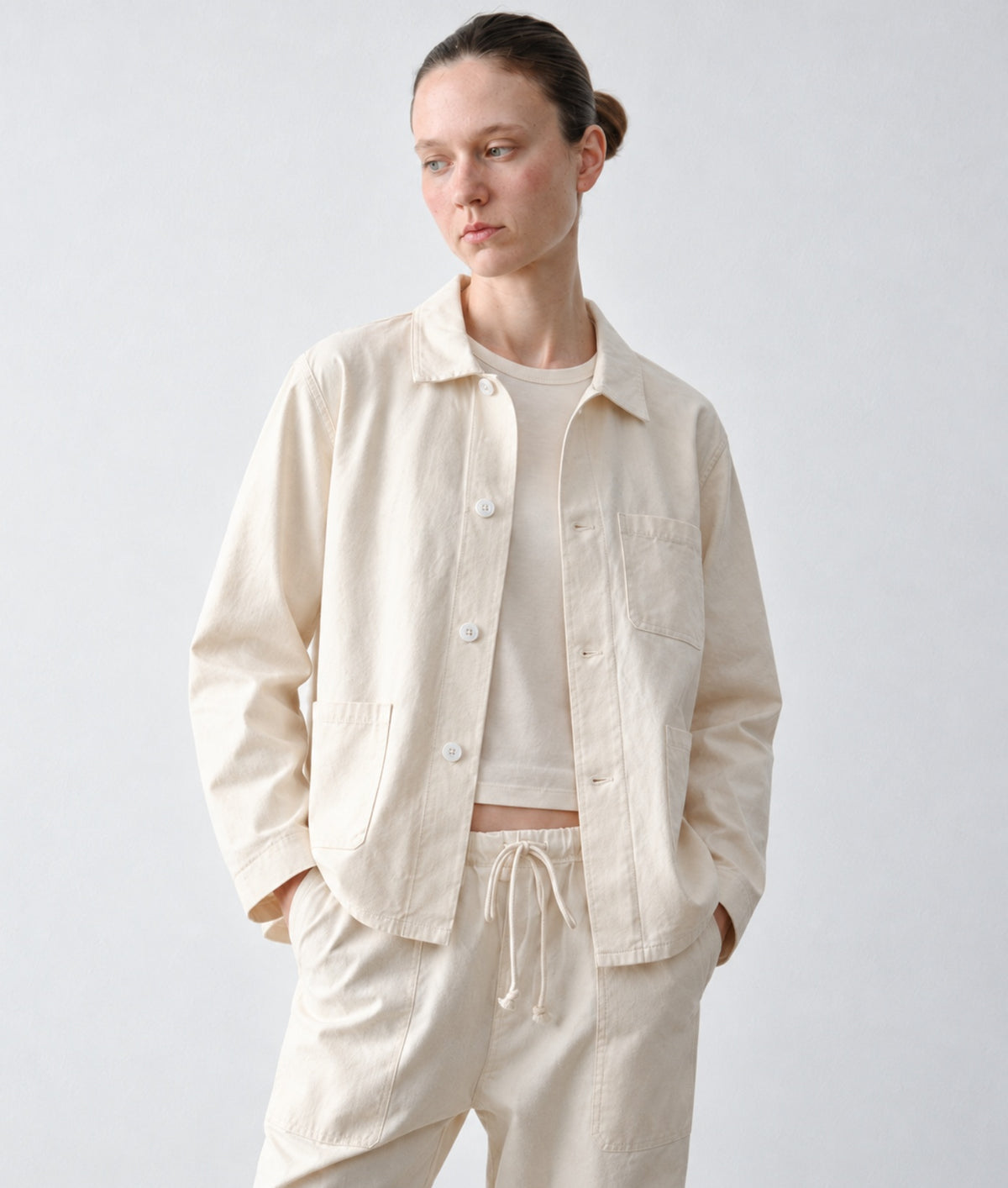 A model wearing IOAN undyed Ponya jacket over a matching crewneck shirt and drawstring trousers, photographed against a neutral light gray studio background.
