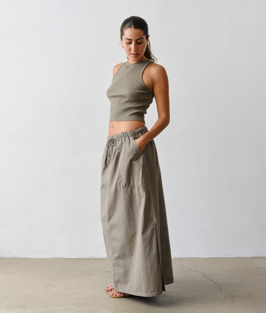 A model standing in a minimalist studio setting wearing the IOAN Ponya Maxi Skirt in Iron 4 and a matching IOAN rib tank.
