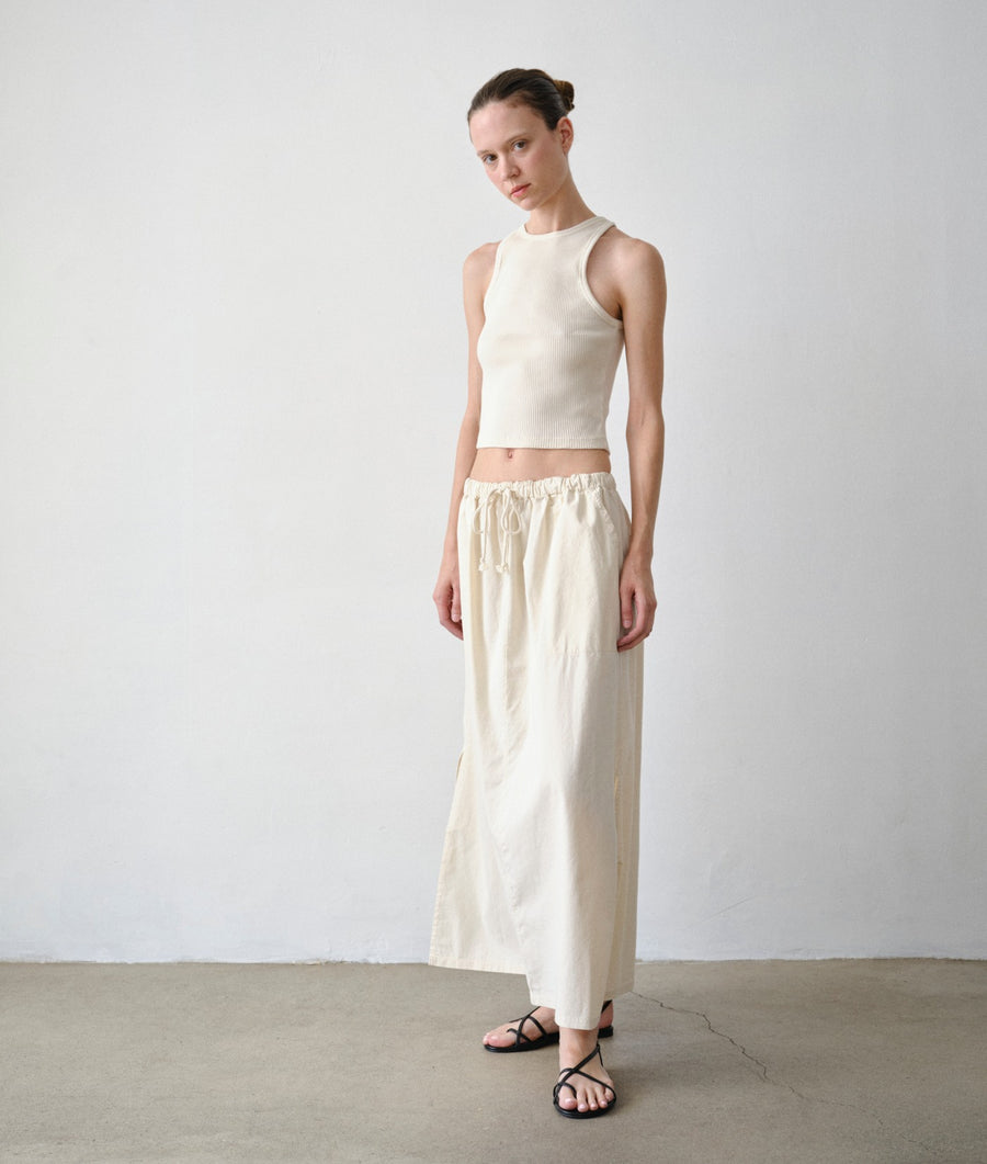 A model standing in a minimalist studio setting wearing the IOAN Ponya Maxi Skirt in undyed and a matching IOAN rib tank.