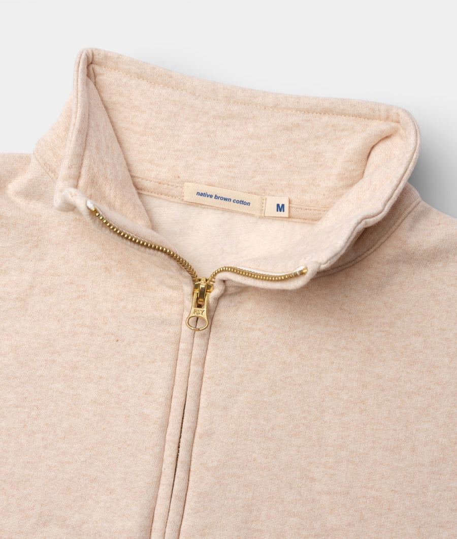 Flat lay detail shot of a beige organic cotton hoodie with a gold zipper from Industry of All Nations.